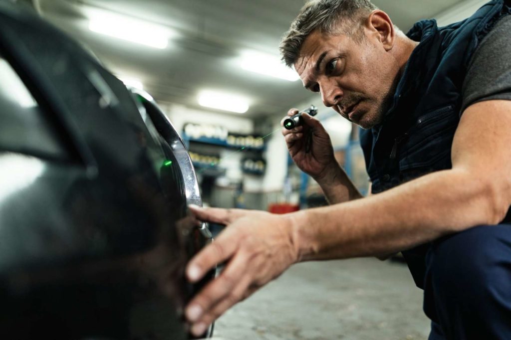 Mid adult mechanic repairing bumper on a car in auto repair shop.